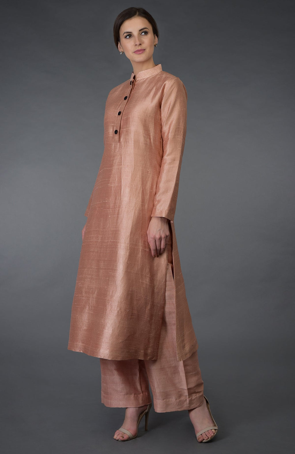 A woman models a pressed rose raw silk suit with a band collar and black buttons.