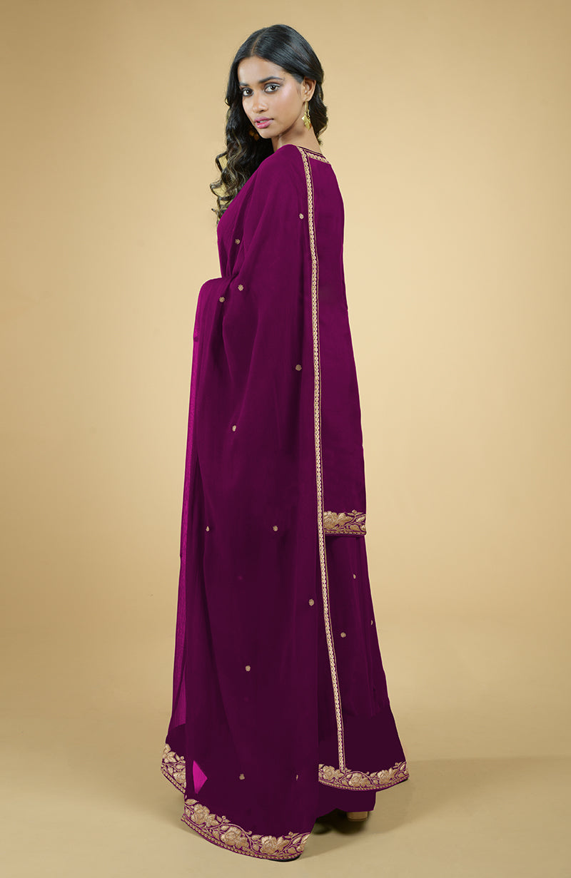A woman in a peacock pink sharara set with gold Kashmiri tilla embroidery.