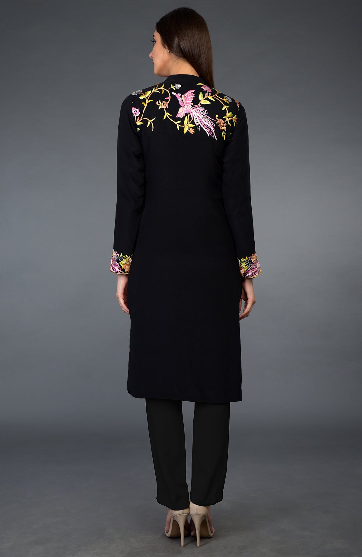 A woman models a black Parsi Gara embroidered jacket suit with floral and bird motifs.