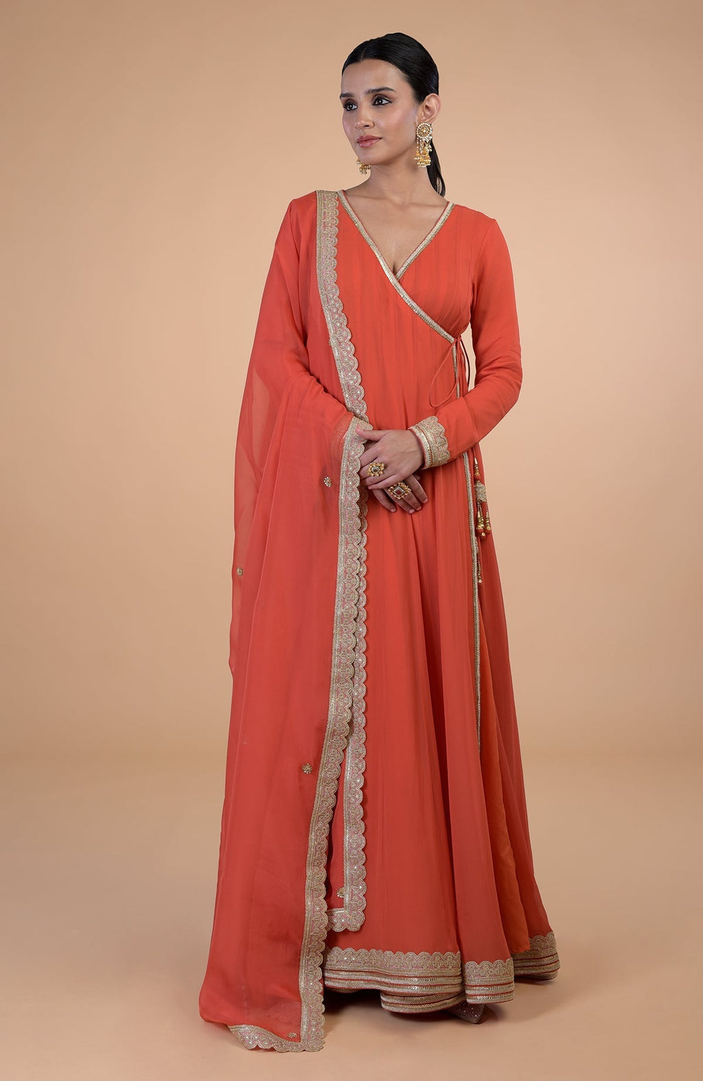 A woman models a burnt orange Angrakha Anarkali set with gold Gota Patti embroidery.