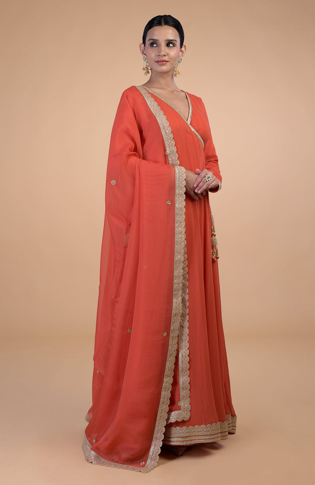 A woman models a burnt orange Angrakha Anarkali set with gold Gota Patti embroidery.