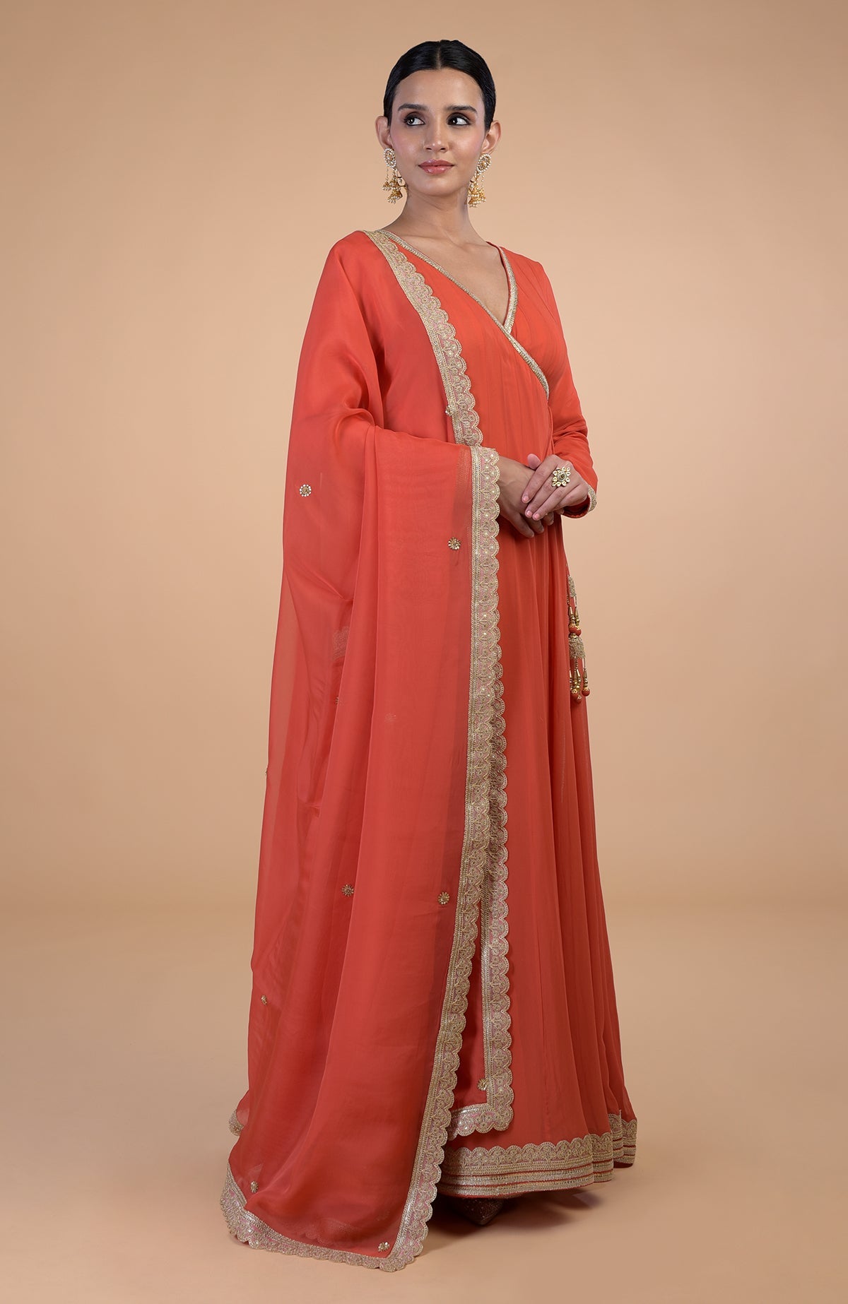 A woman models a burnt orange Angrakha Anarkali set with gold Gota Patti embroidery.