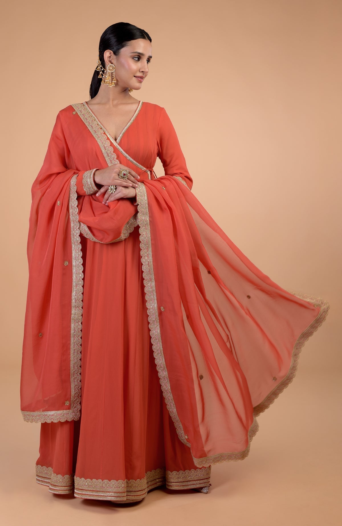 A woman models a burnt orange Angrakha Anarkali set with gold Gota Patti embroidery.