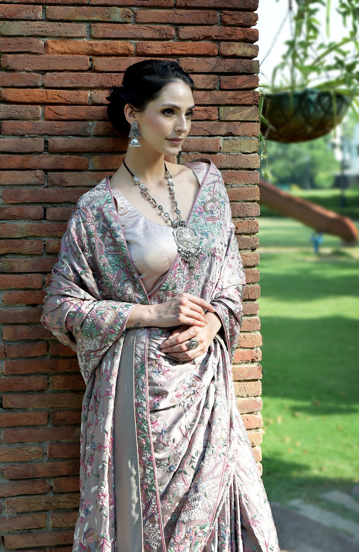 A woman models a tea rose Parsi Gara hand-embroidered saree with a silver necklace.