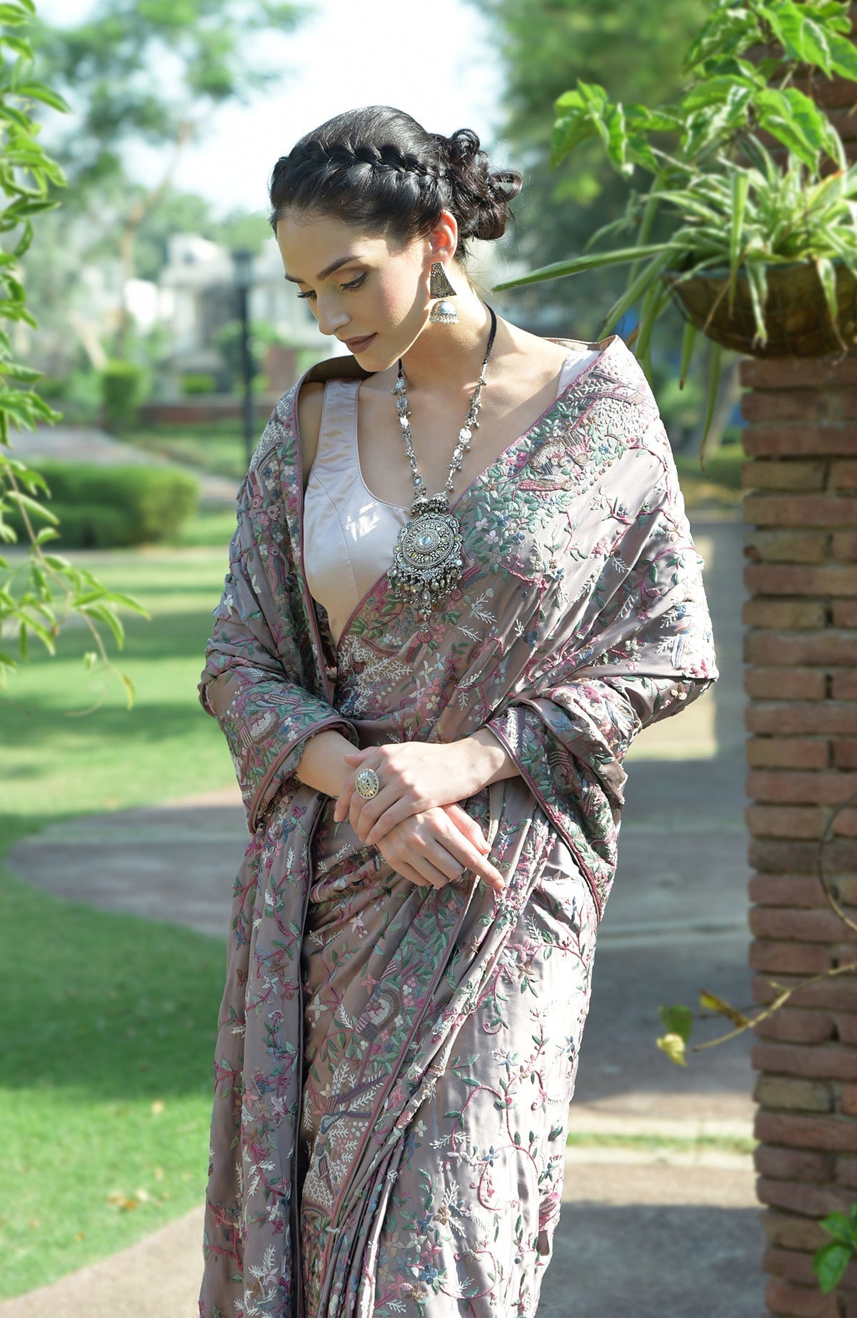 A woman models a tea rose Parsi Gara hand-embroidered saree with a long necklace.