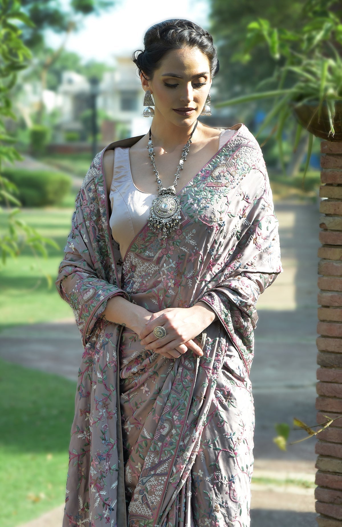 A woman models a tea rose Parsi Gara hand-embroidered saree with a silver necklace.