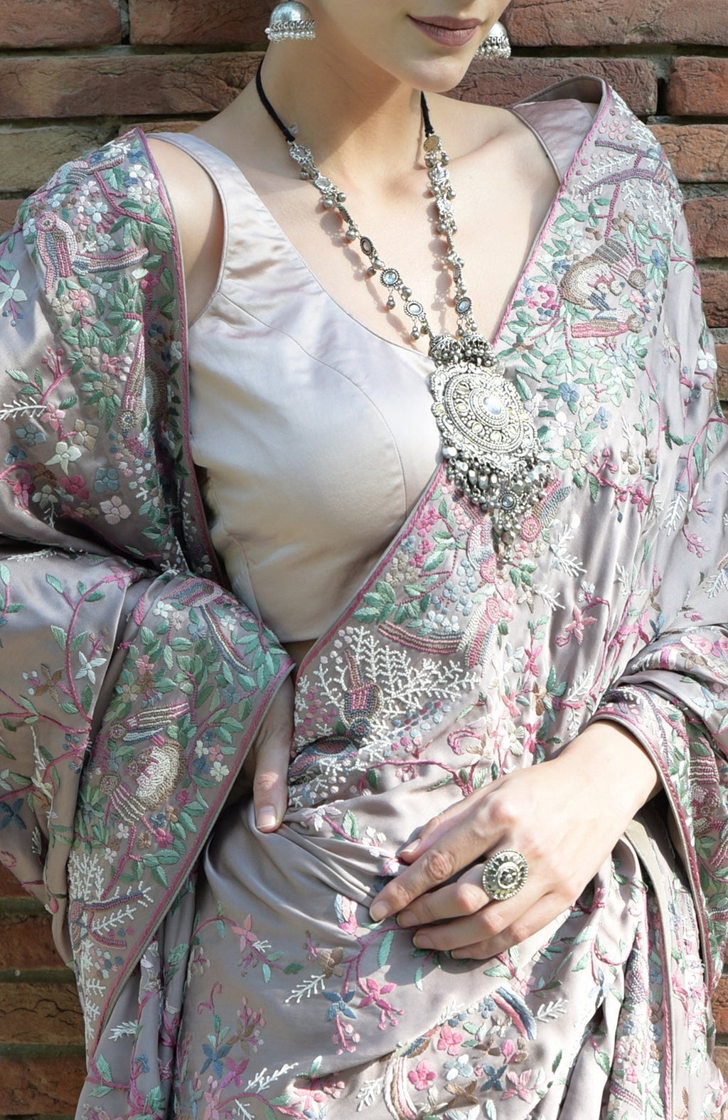A woman models a tea rose Parsi Gara hand-embroidered saree with a silver necklace.