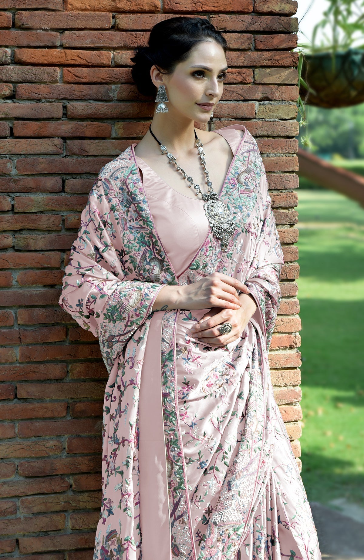 A woman in a pale pink Parsi Gara hand-embroidered saree with a long silver necklace.