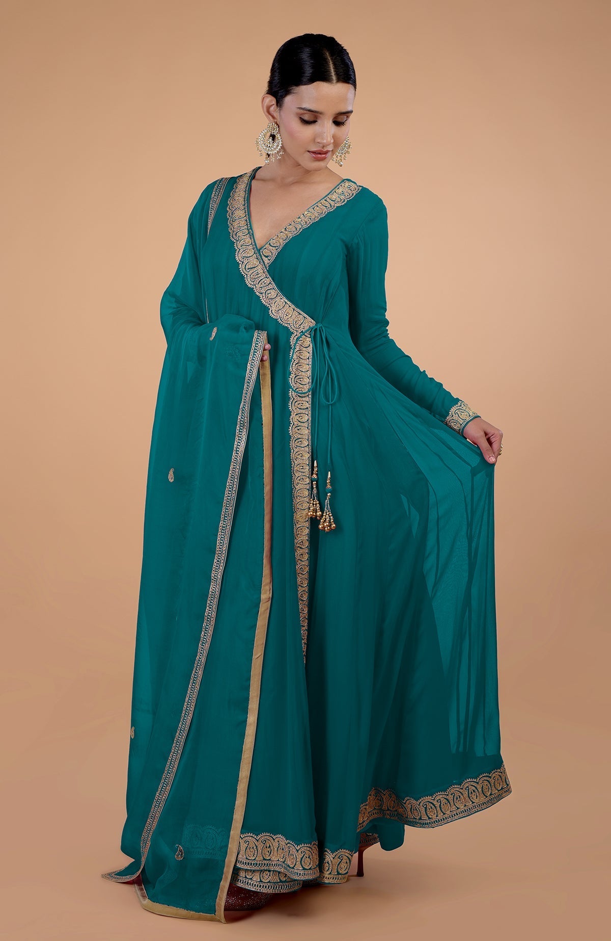A woman models a teal blue angrakha anarkali set with gold paisley embroidery.