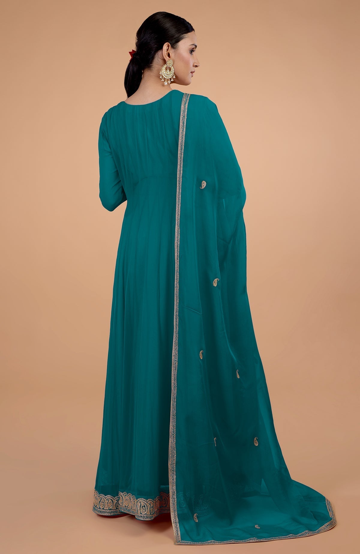 A woman in a teal blue anarkali set with gold paisley embroidery.