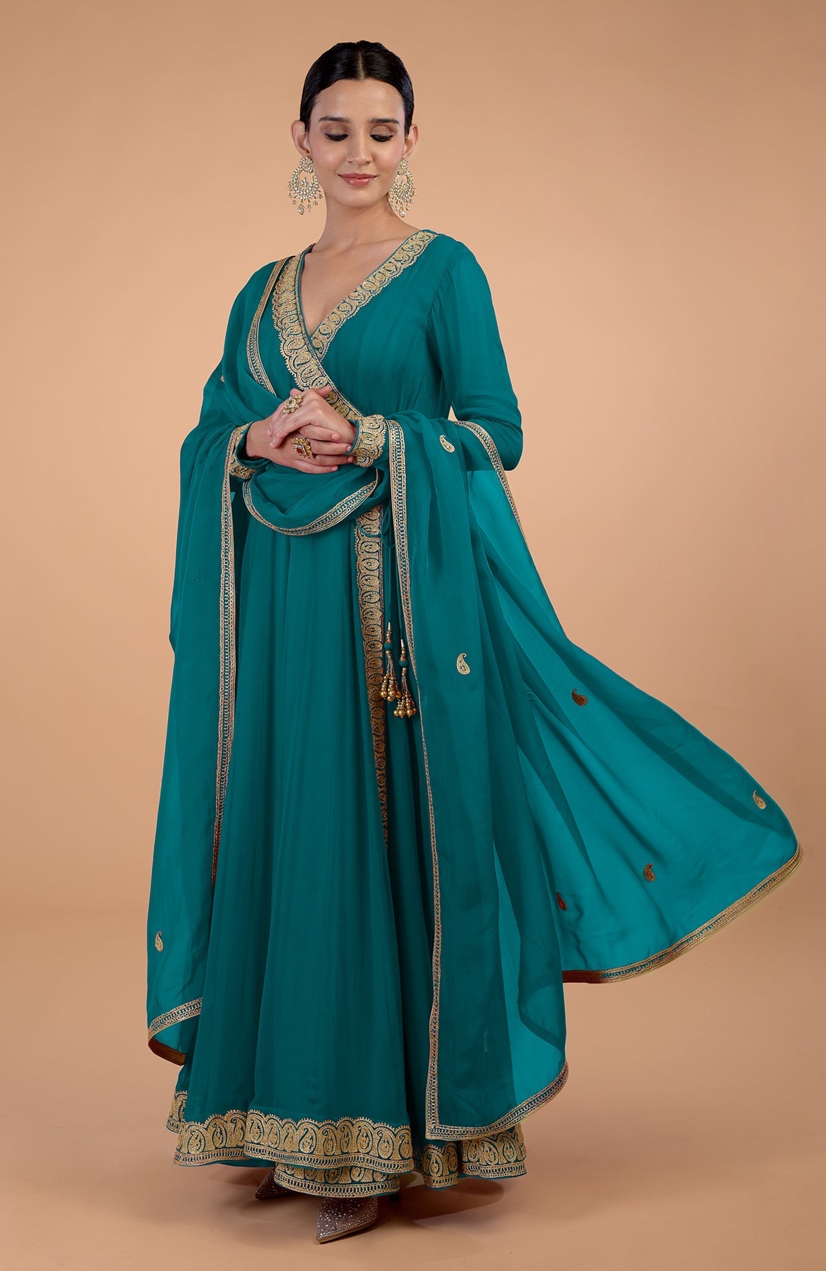 A woman in a teal angrakha anarkali set with gold embroidery and a matching dupatta.