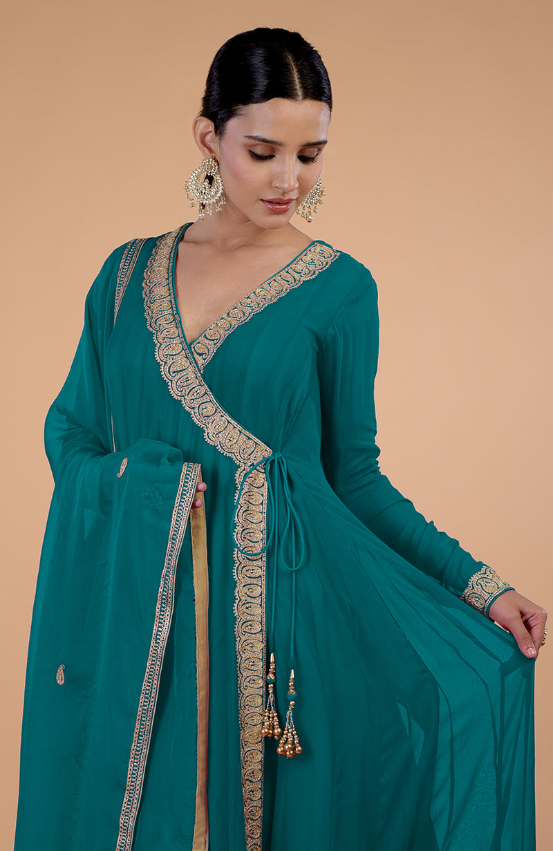 A woman models a teal blue angrakha anarkali set with gold paisley embroidery.