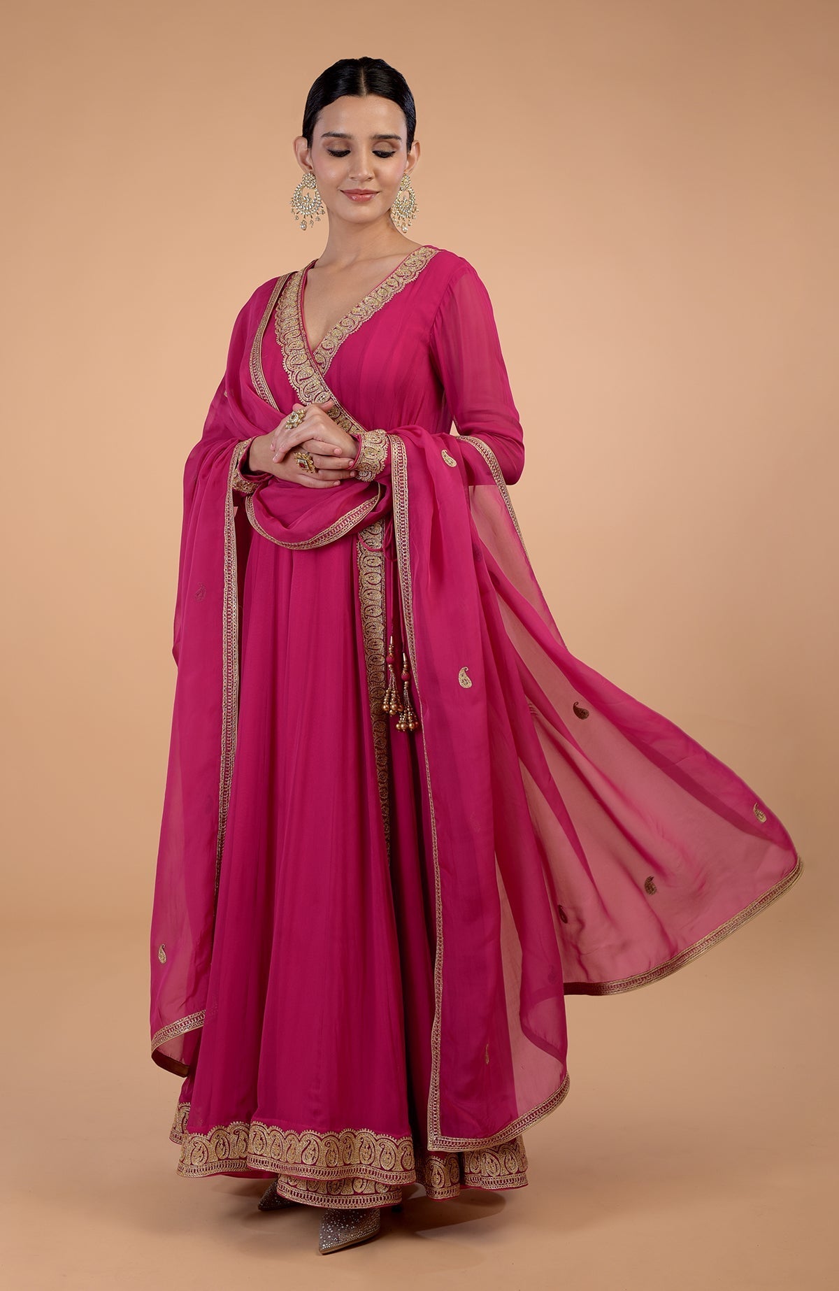 A woman models a raspberry pink Angrakha Anarkali set with gold paisley embroidery.
