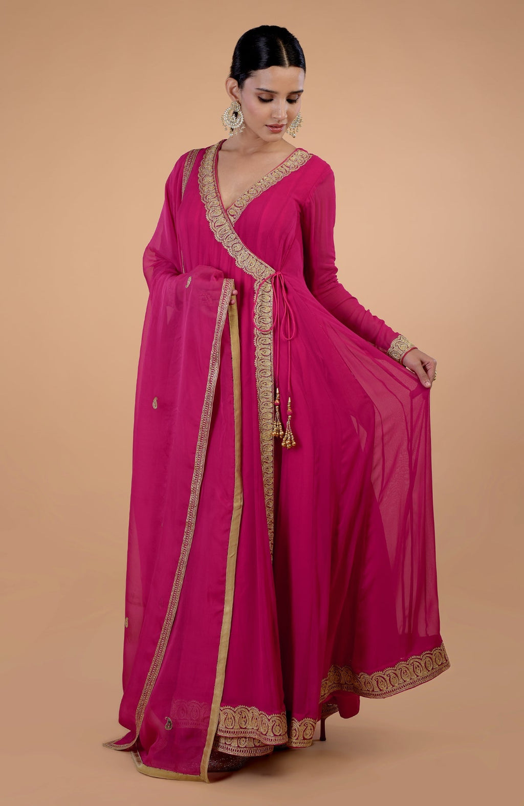A woman models a raspberry pink angrakha anarkali set with gold Kashmiri Tilla embroidery.
