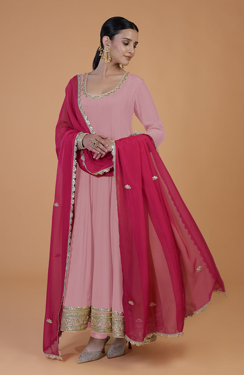 A woman models a pink anarkali set with a fuchsia dupatta and gold embroidery.