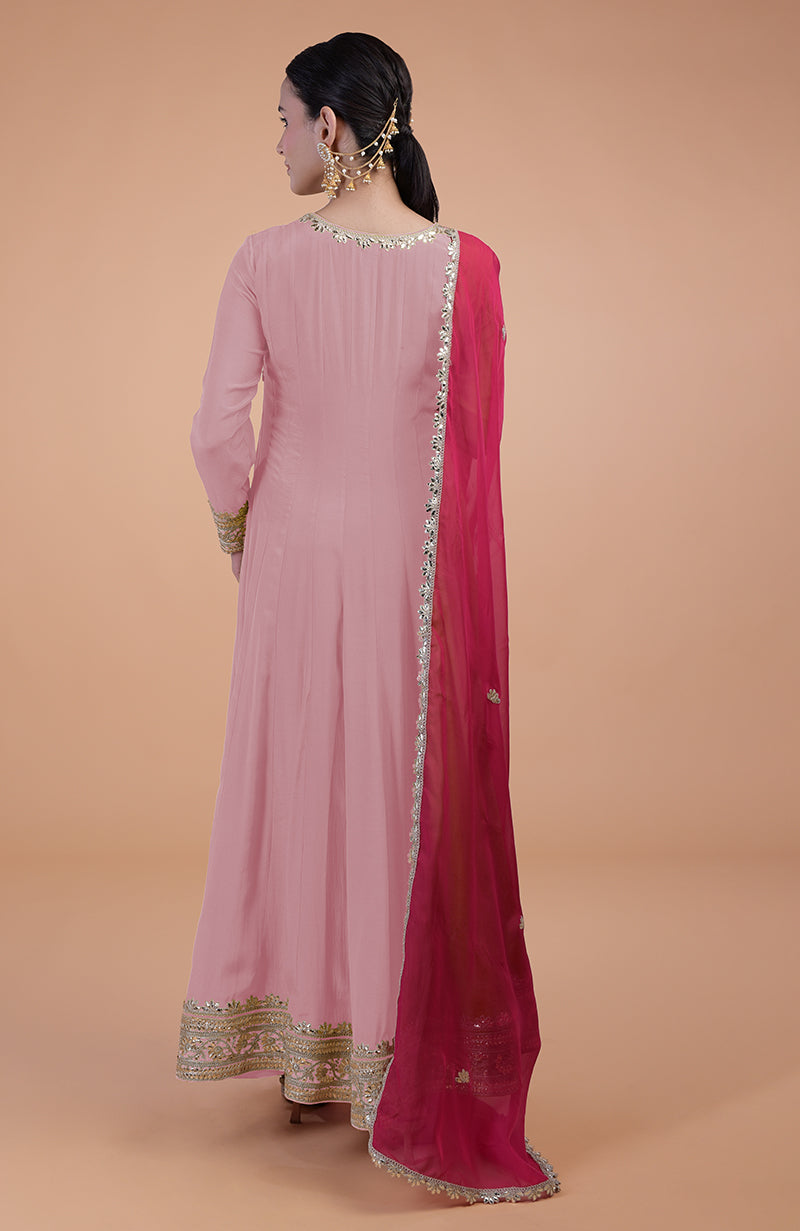 A woman from behind wears a pink anarkali set with gold embroidery and a fuchsia dupatta.