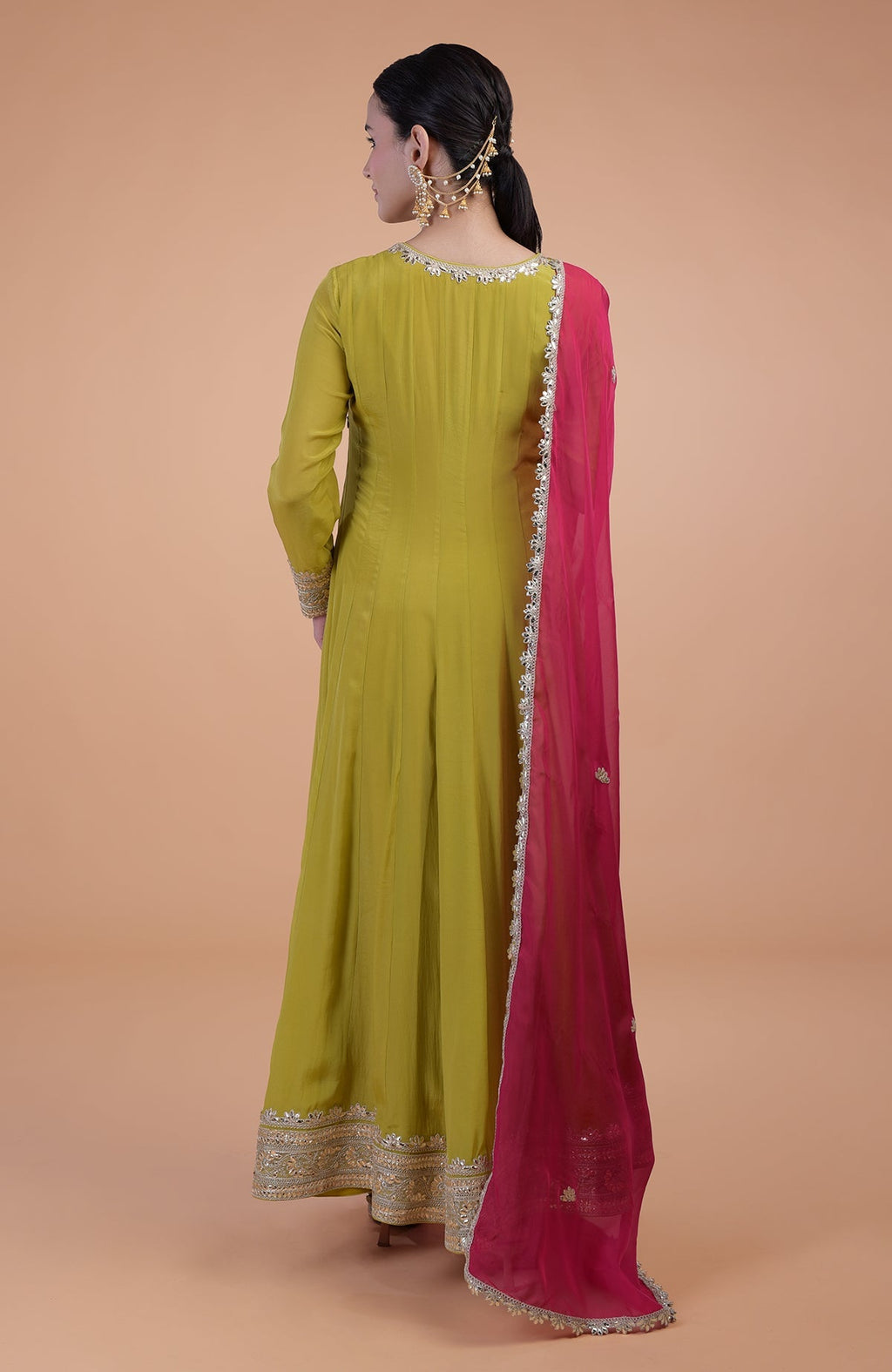 A woman from behind wearing a green Anarkali suit with a pink dupatta.
