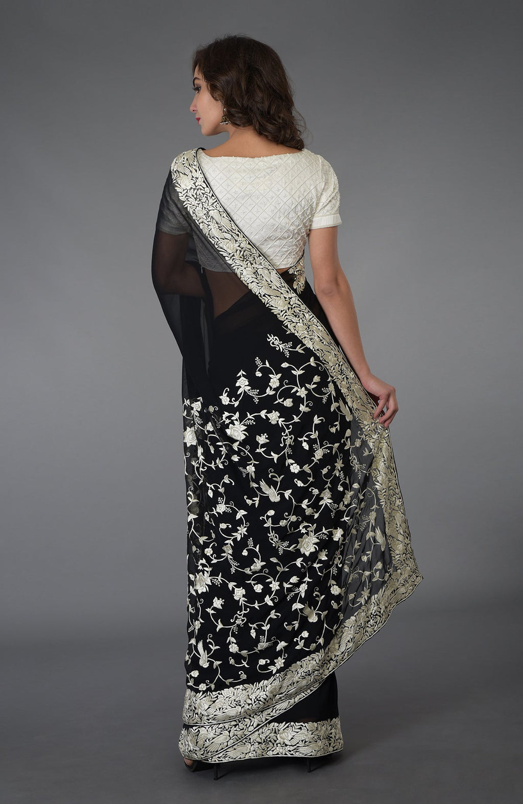 A woman models a black and ivory Parsi Gara hand-embroidered saree with floral and bird motifs.