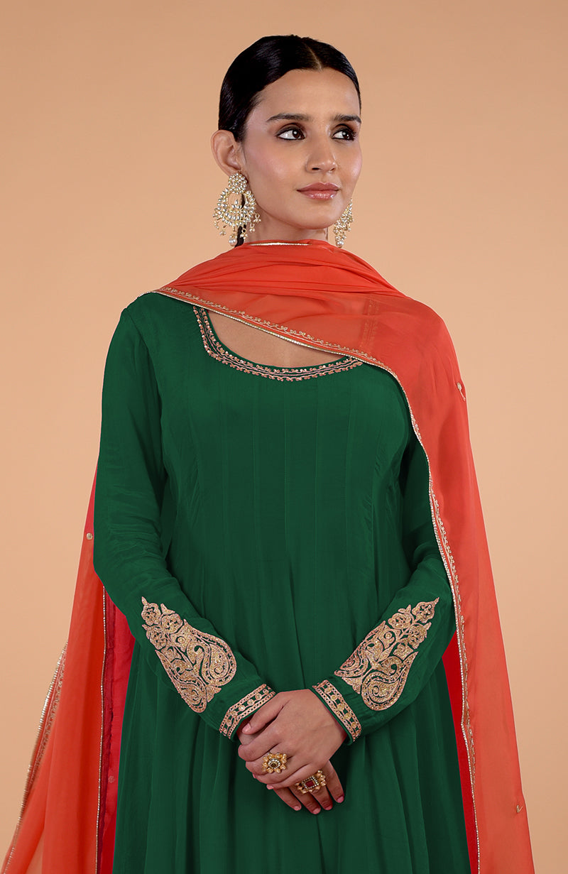 A woman in a bottle green anarkali set with an orange dupatta.