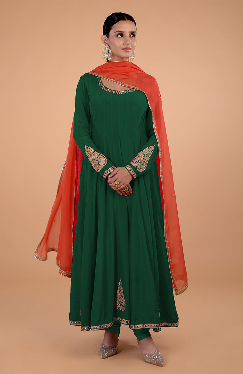 A woman models a bottle green anarkali set with an orange dupatta.