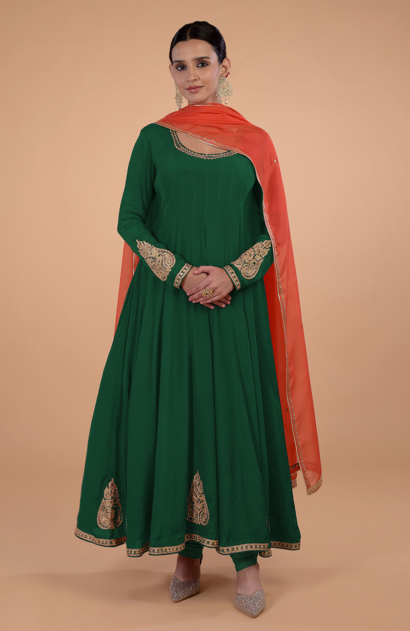 A woman in a green anarkali suit with an orange dupatta and gold embroidery.