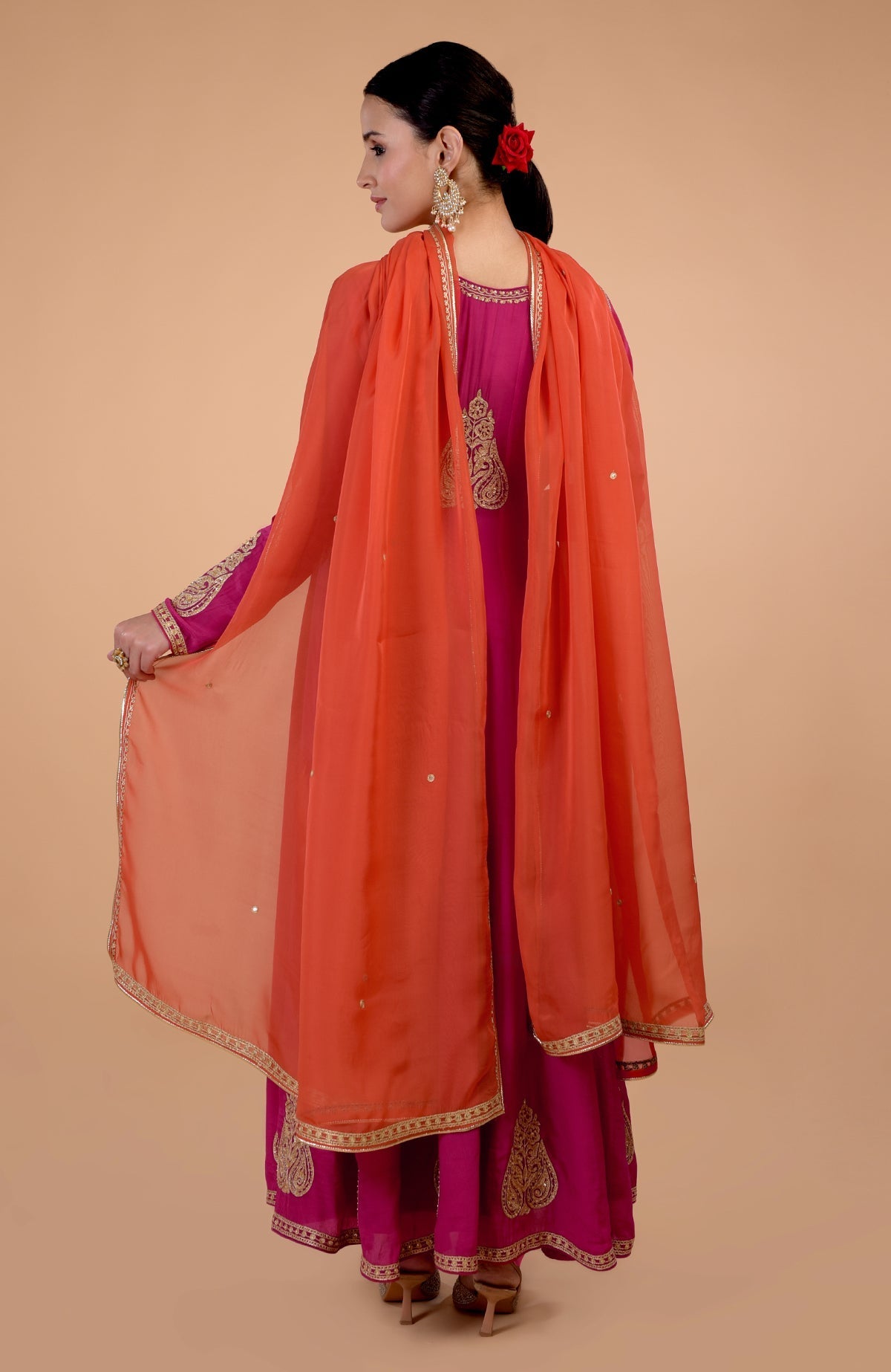 A woman models a raspberry pink Anarkali set with an orange dupatta.