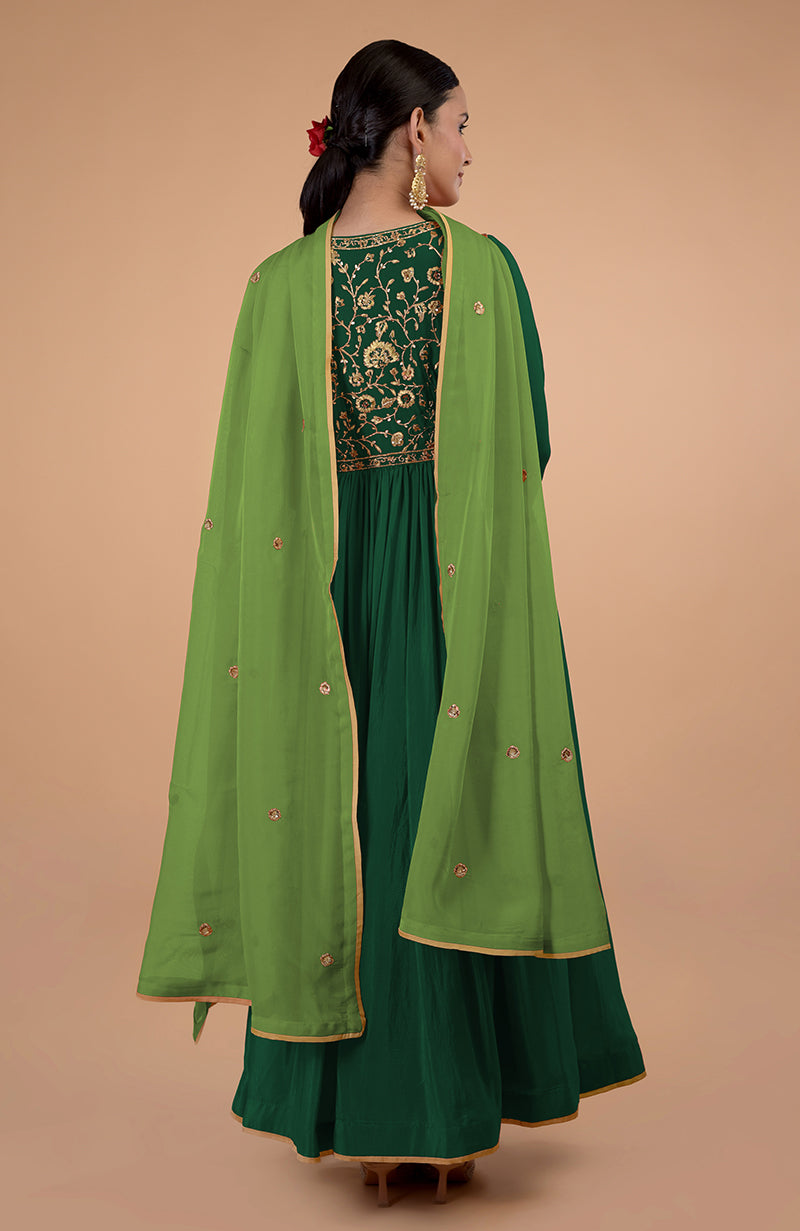 A woman from behind wears a bottle green anarkali with gold embroidery and a sheer green dupatta.