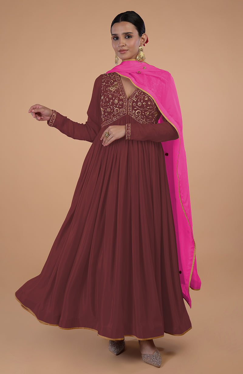 A woman models a marsala anarkali with gold embroidery and a pink dupatta.