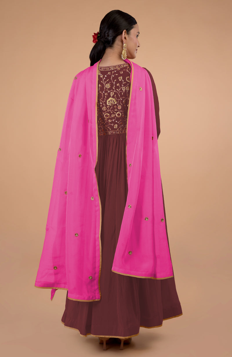 A woman models a marsala anarkali with gold embroidery and a pink dupatta.