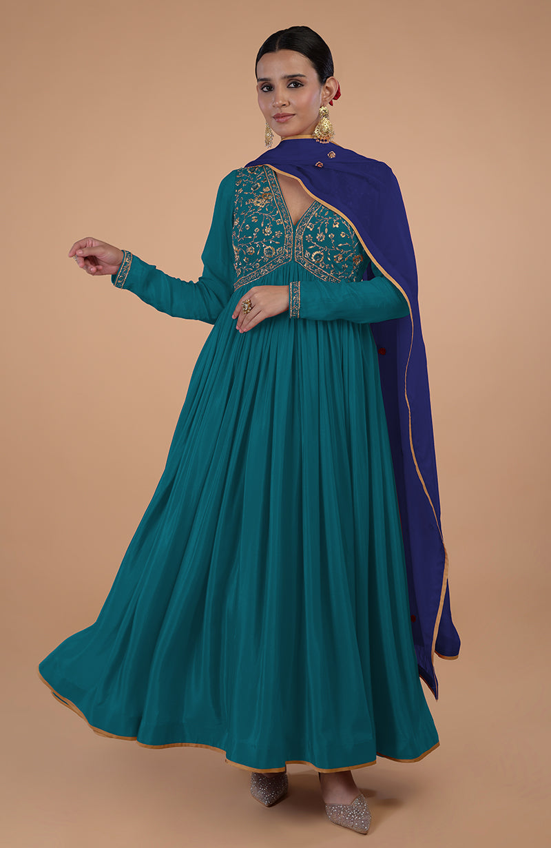 A woman models a teal-blue anarkali set with gold embroidery and a royal blue dupatta.