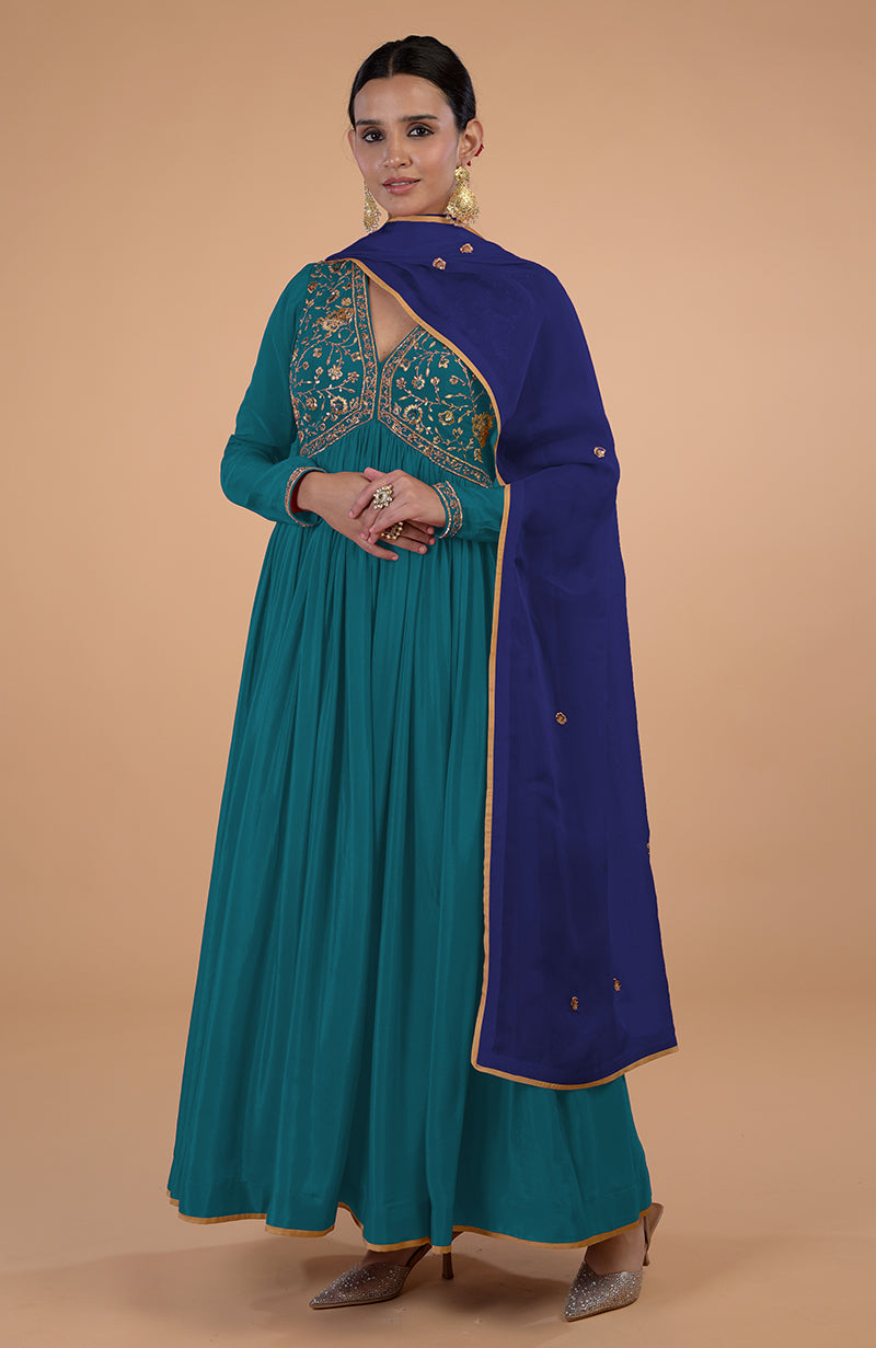A woman models a teal-blue anarkali set with gold embroidery and a royal blue dupatta.