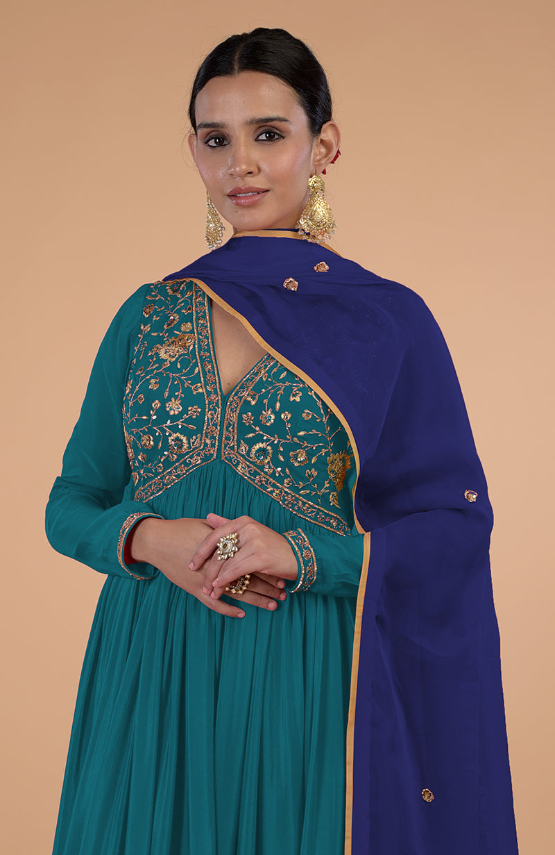 A woman models a teal-blue zardozi and resham embroidered anarkali set with a blue dupatta.