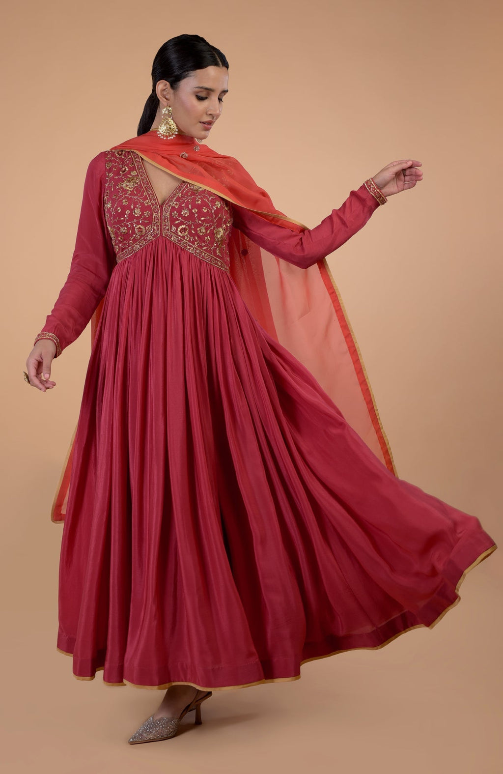 A woman models a red-orange zardozi and resham embroidered anarkali set.