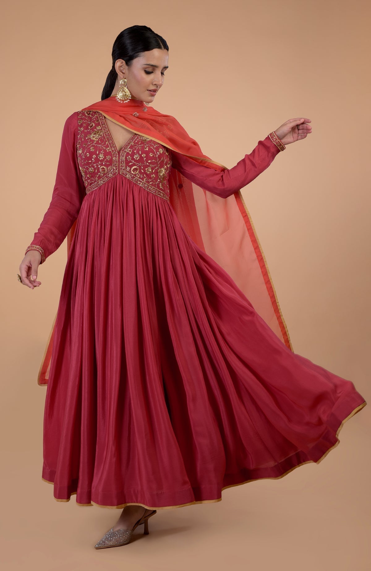 A woman models a red-orange zardozi and resham embroidered anarkali set.