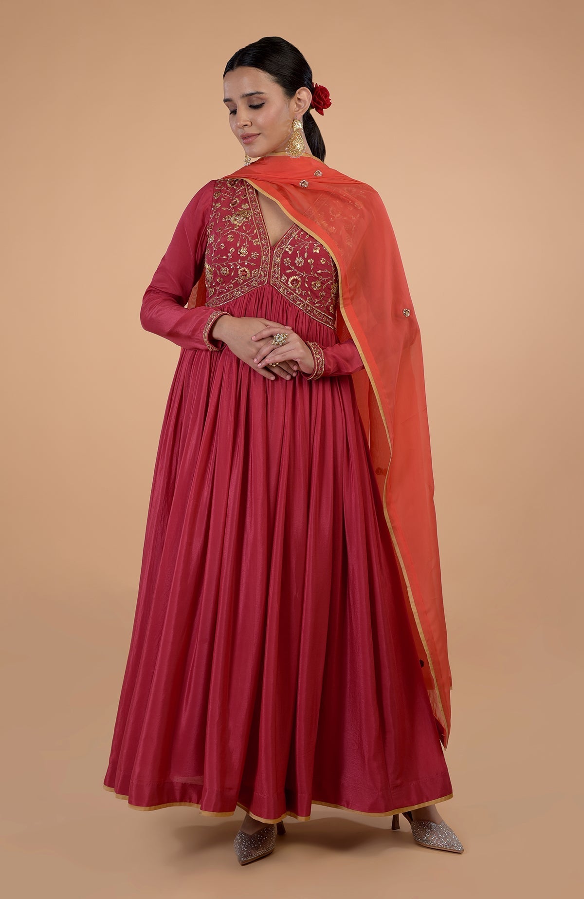 A woman models a red embroidered Anarkali set with an orange dupatta.