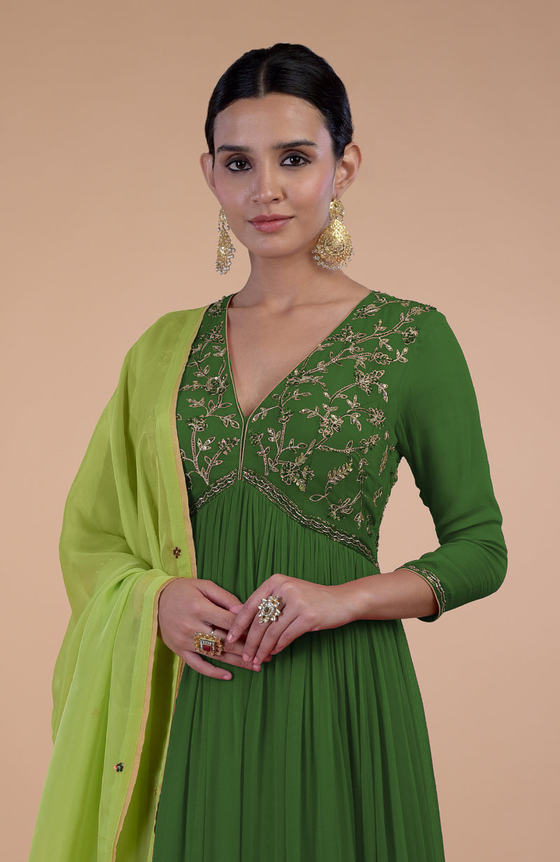 A woman in a green embroidered anarkali set with a matching dupatta and gold earrings.