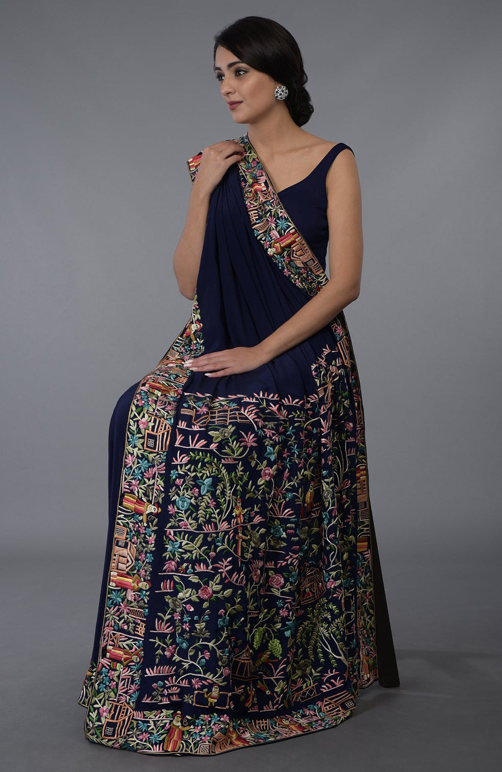 A woman sits wearing a midnight blue Parsi Gara hand-embroidered saree.