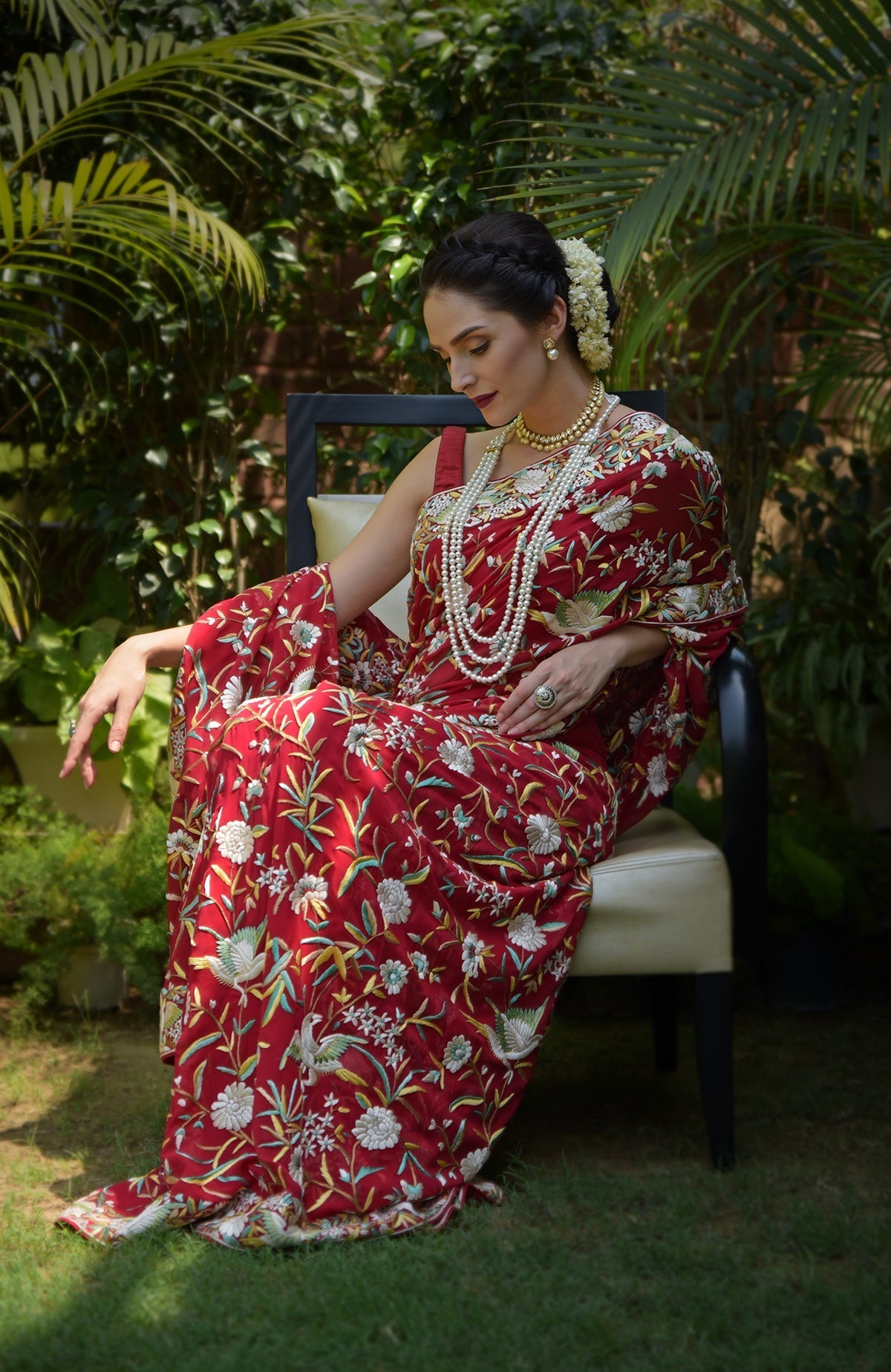 A woman in a red Parsi Gara hand-embroidered saree with floral and bird motifs.