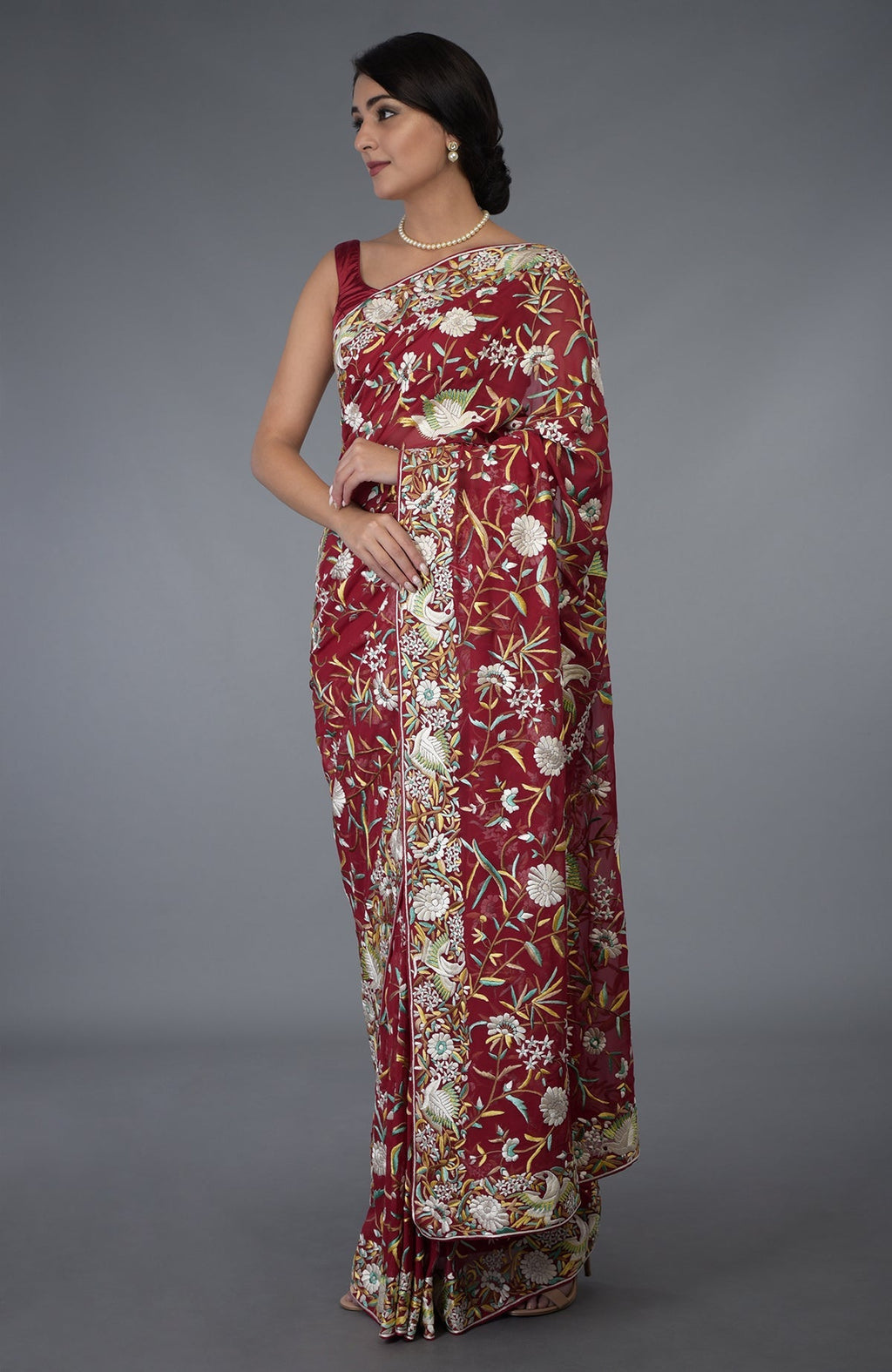 A woman models a red Parsi Gara hand-embroidered saree with floral and bird motifs.