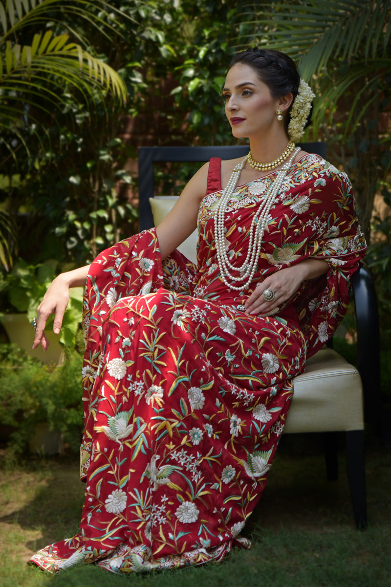 A woman in a red Parsi Gara hand-embroidered saree with floral and bird motifs.