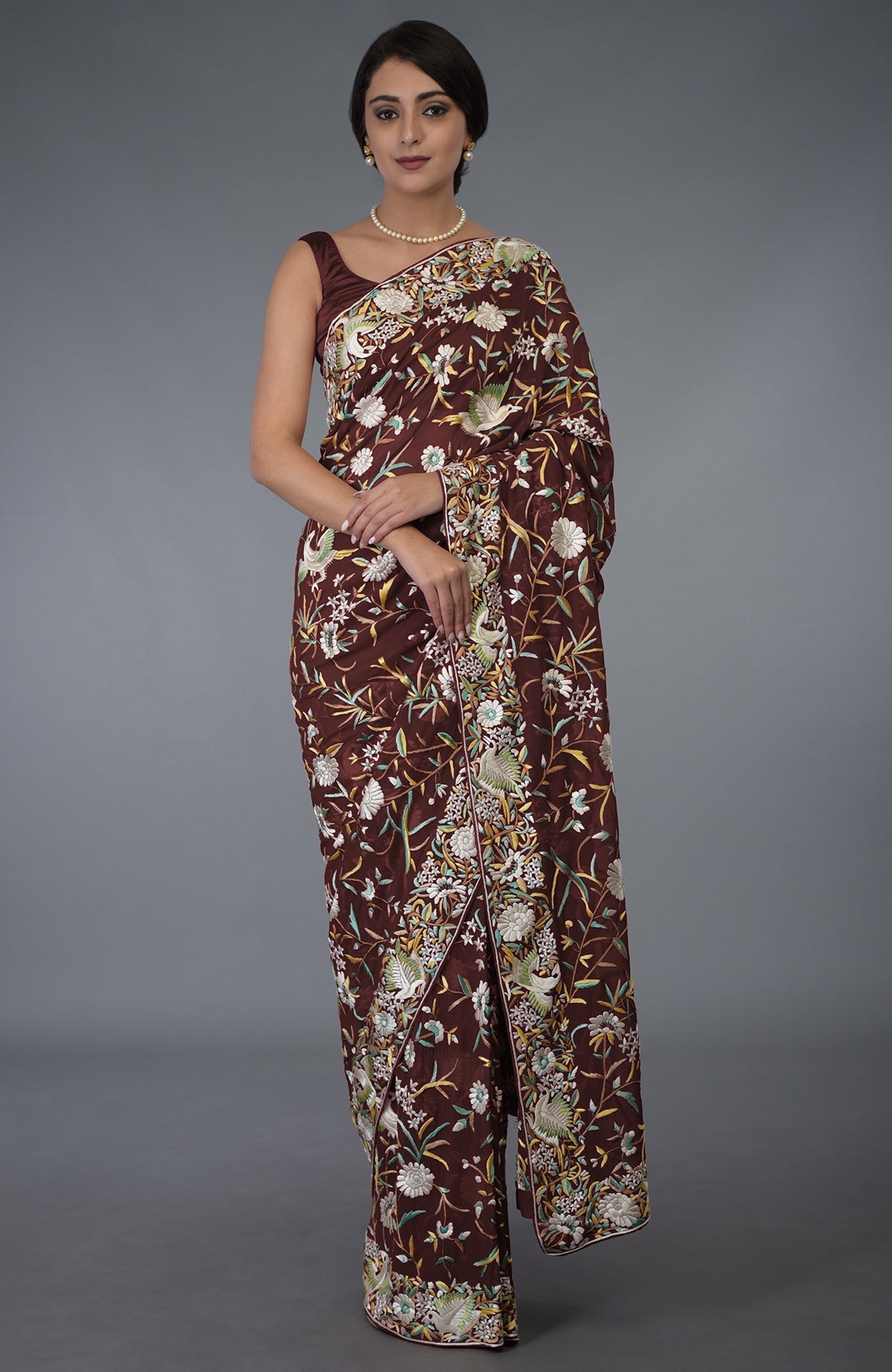 A woman models a marsala Parsi Gara hand-embroidered saree with floral and bird motifs.