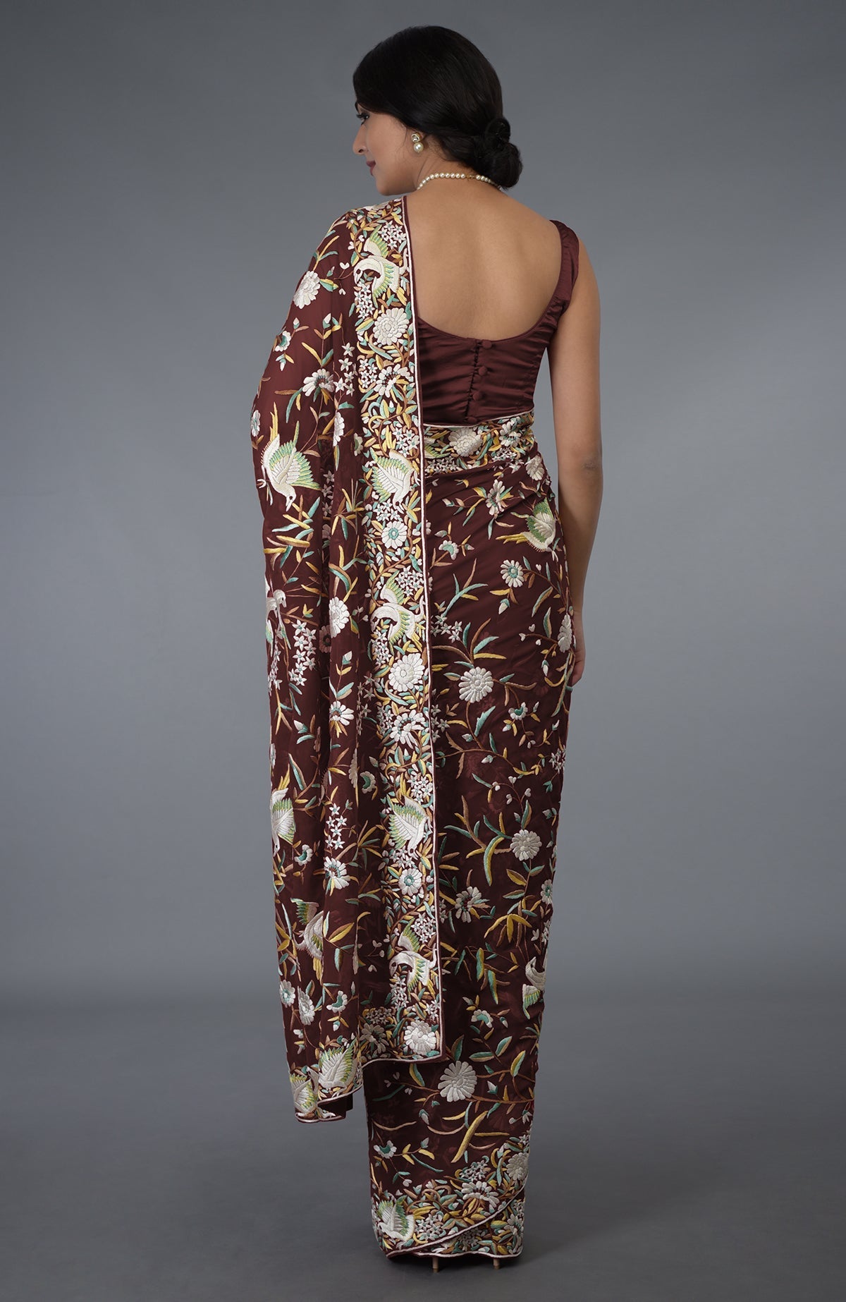 A woman from behind models a marsala Parsi Gara hand-embroidered saree with floral and bird patterns.