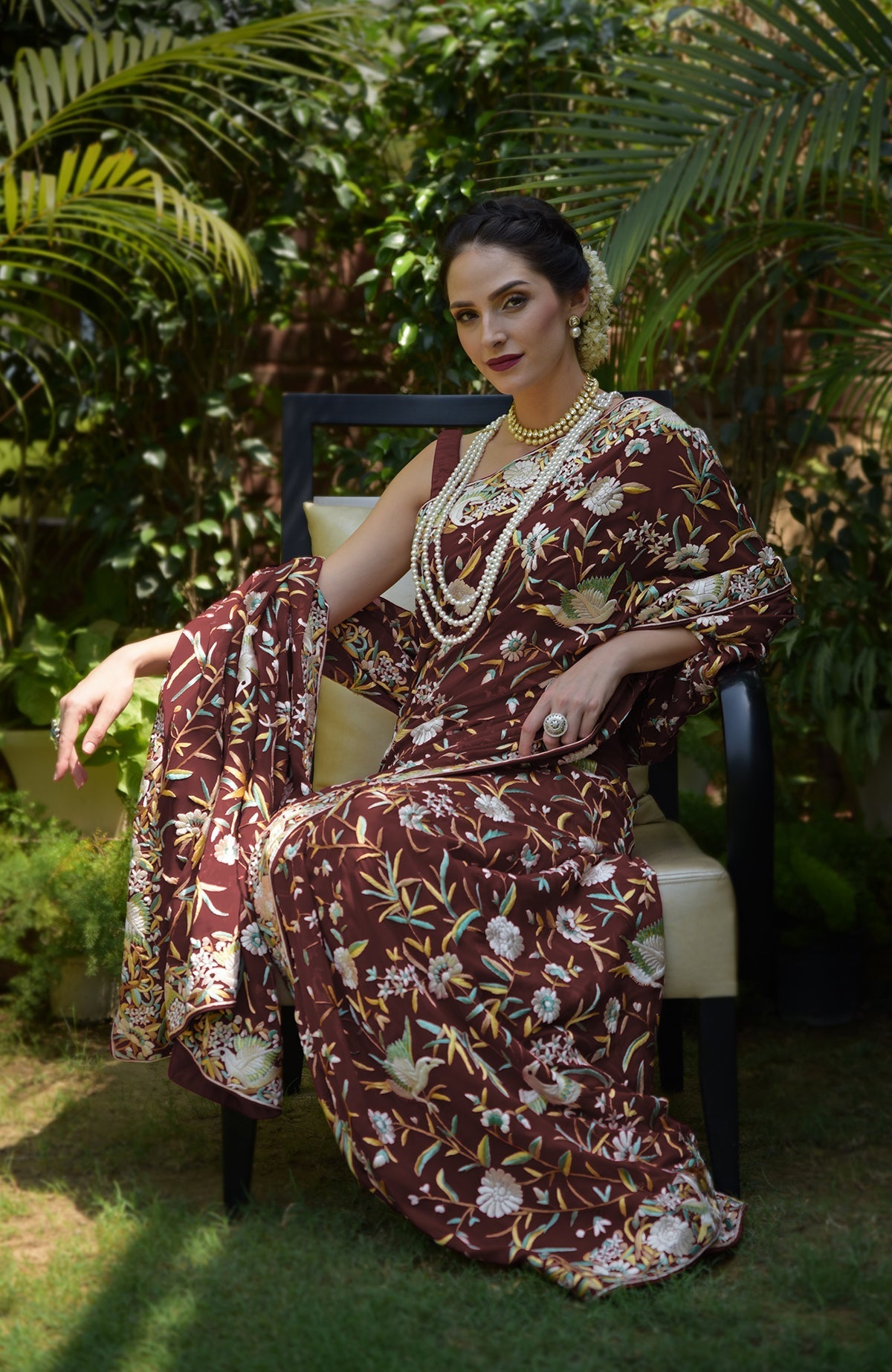 A woman in a marsala Parsi Gara hand-embroidered saree with bird and floral motifs.