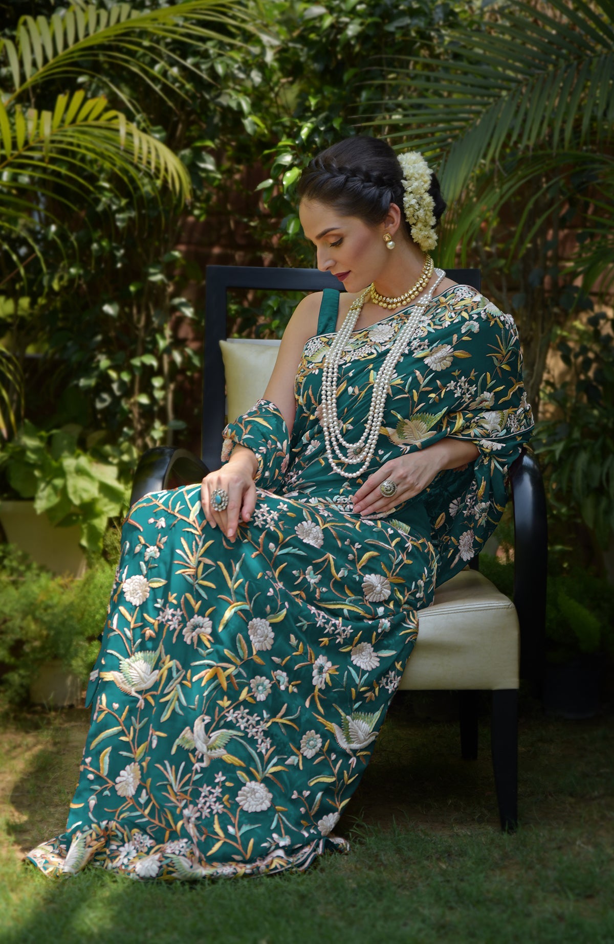 A woman in a teal Parsi Gara hand-embroidered saree with bird and floral motifs.