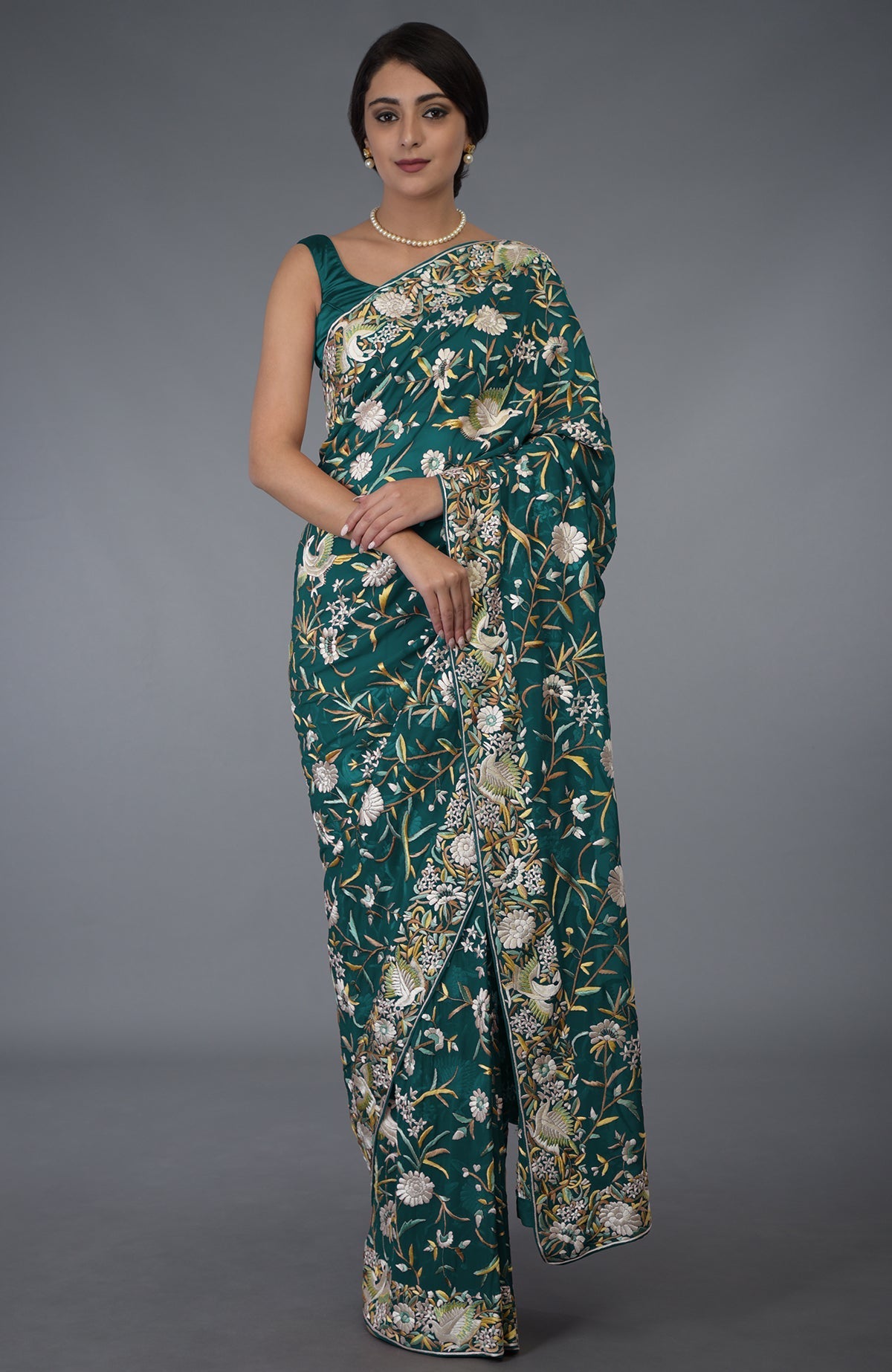 A woman models a teal Parsi Gara hand-embroidered saree with floral and bird motifs.