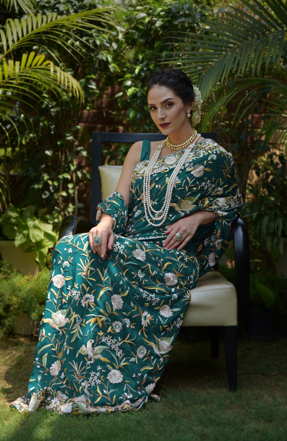 A woman in a green Parsi Gara hand-embroidered saree with birds and floral patterns.