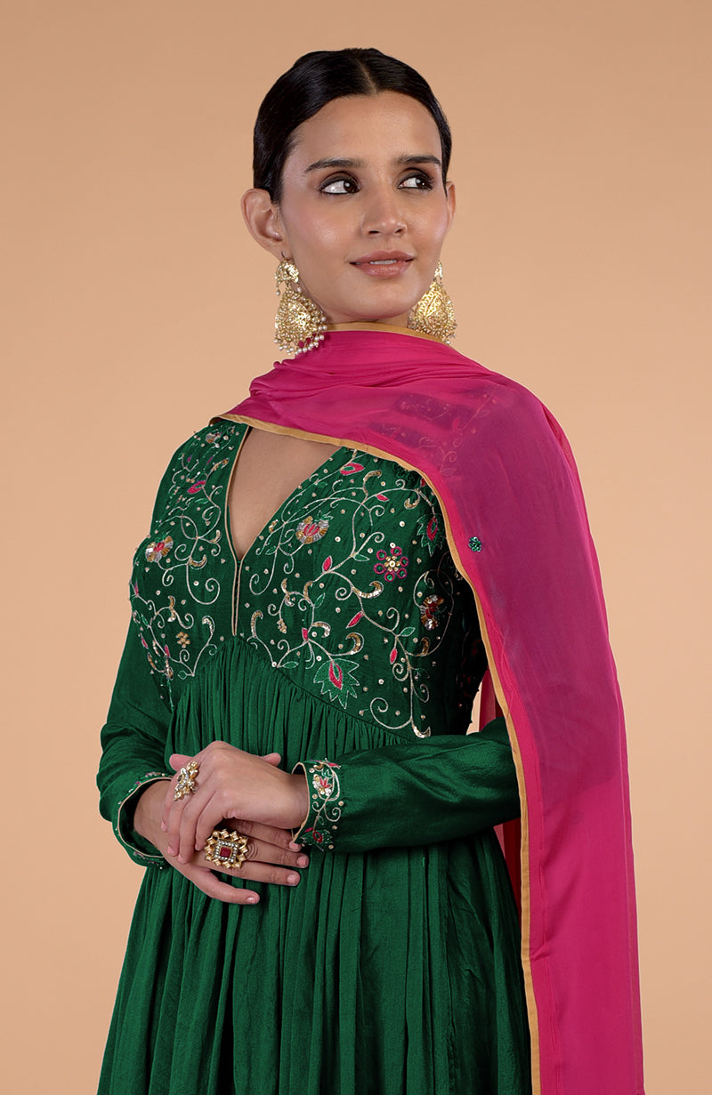 A woman models a bottle green anarkali set with a pink dupatta and gold earrings.