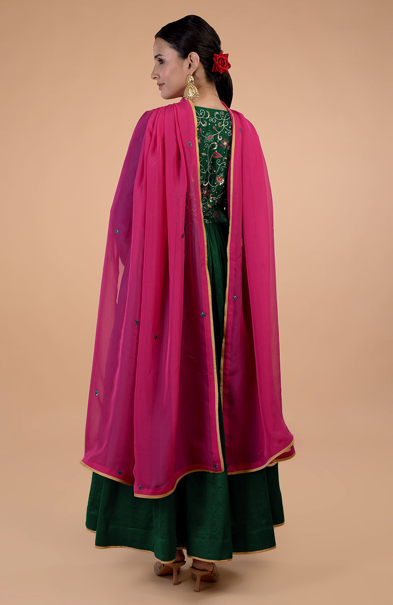 A woman in a bottle green anarkali with a pink dupatta and zardozi embroidery.