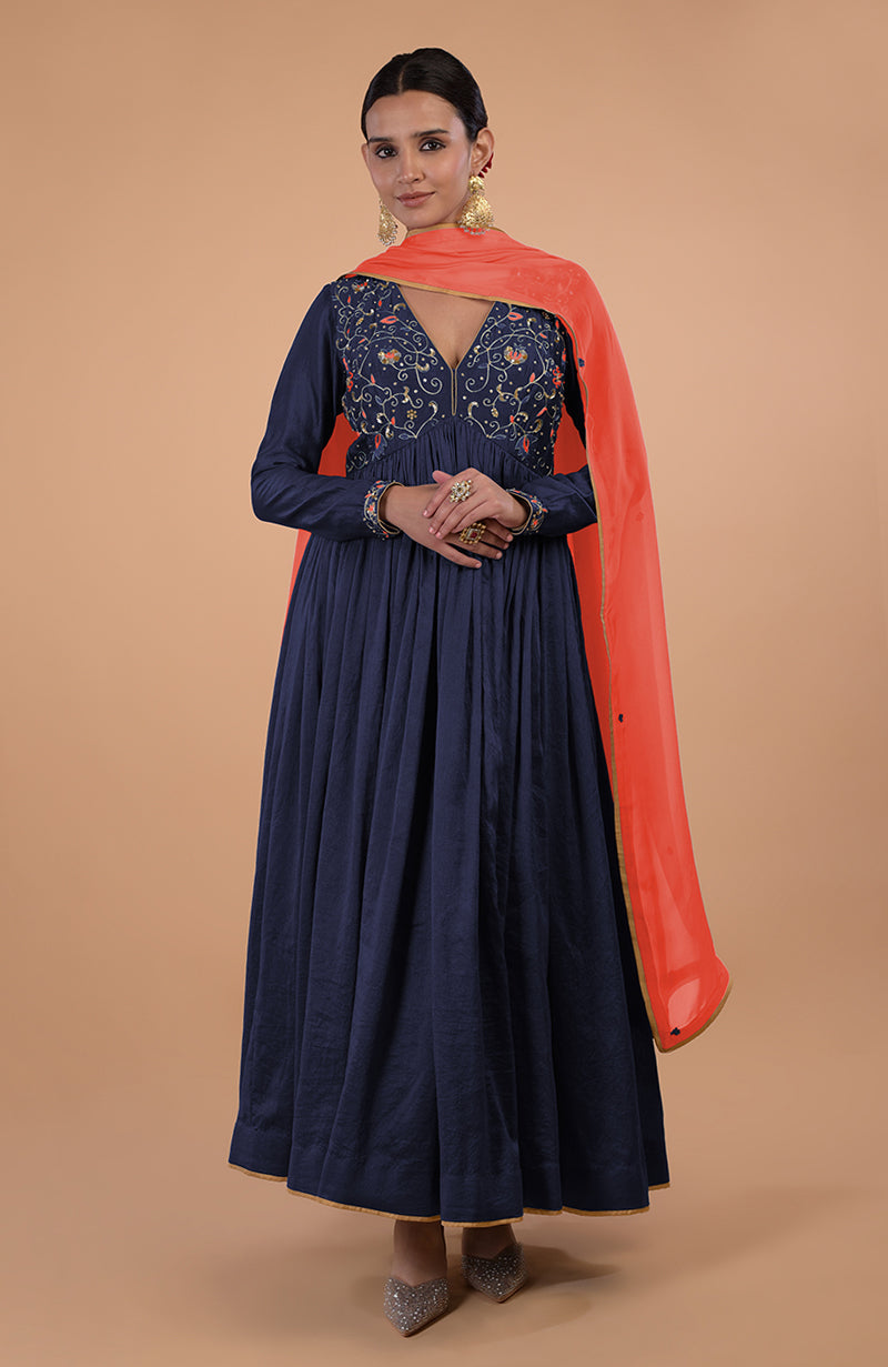 A woman in a navy blue embroidered anarkali with an orange dupatta and embellished shoes.