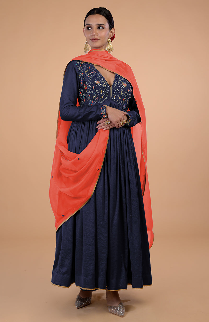 A woman models a navy blue anarkali with orange dupatta and gold embroidery.